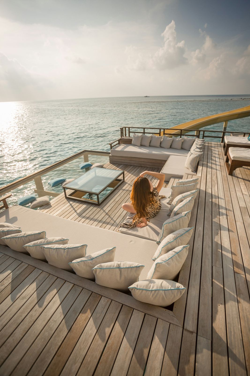 A guest relaxing on an overwater deck lounge at golden hour