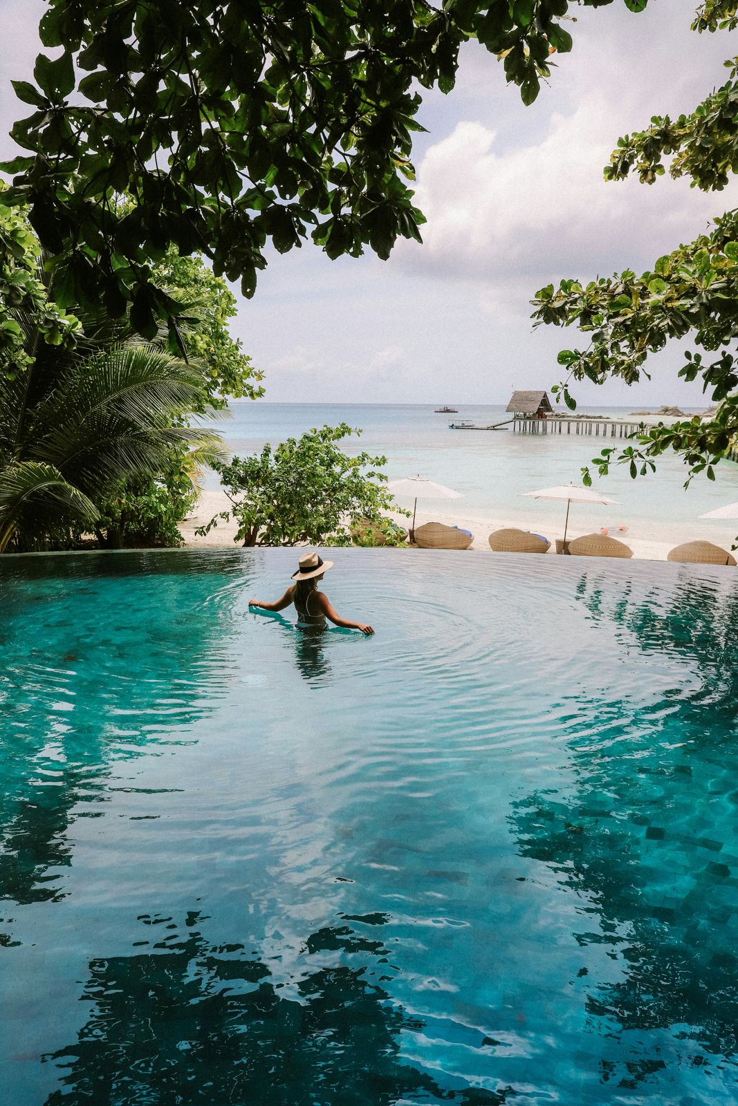 A guest resting in an infinity pool overlooking a tropical bay